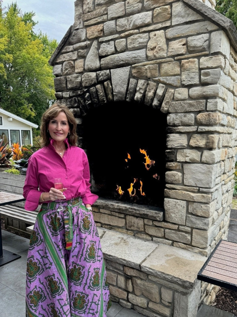 Model is wearing Ruffle Shirt Long Sleeve Berry standing in front of fireplace holding a glass of champagne.